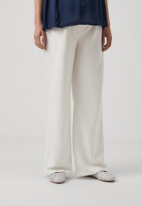 White wide-leg trousers made from a soft fabric, paired with silver embellished slip-on shoes with a textured surface.