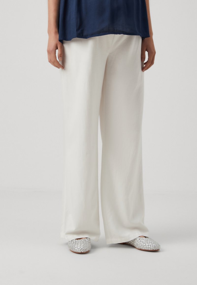 White wide-leg trousers made from a soft fabric, paired with silver embellished slip-on shoes with a textured surface.