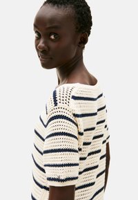 Szydełkowany sweter w kolorze kremowym z granatowymi paskami. Posiada krótkie rękawy, szeroki dekolt oraz otwartą strukturę tkanki.