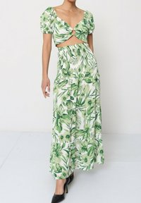 Ensemble floral vert en deux pièces comprenant un haut court avec des manches bouffantes et une jupe maxi à volants taille haute. Tissu texturé, finition lisse.