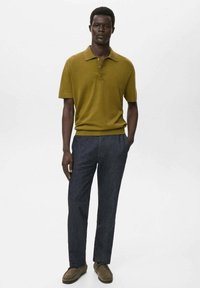 Olivgrön kortärmad polotröja med krage, i kombination med mörkblå byxor och bruna mockaskor. Ren, minimalistisk design.