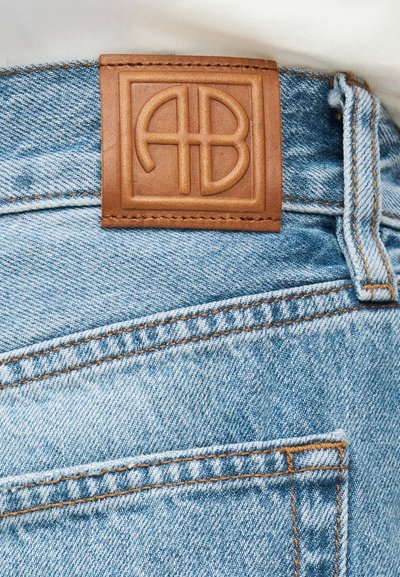 Világoskék farmernadrág látható hátsó zsebbel és a zseb fölött barna bőr folttal, amelyen dombornyomott "AB" logó található.