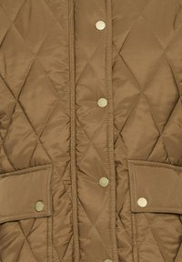 Tissu matelassé marron avec coutures en diamant, avec des boutons-pression en métal et des poches à rabat sur une veste ou un manteau.