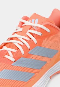 Φωτεινό κοραλί αθλητικό παπούτσι με λευκά κορδόνια, πλέγμα στο πάνω μέρος και τρεις γκρι λαστιχένιες λωρίδες στο πλάι για επιπλέον λεπτομέρεια.