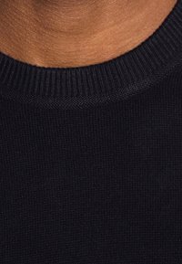 Schwarzer Strickpullover mit rundem Halsausschnitt, der eine gerippte Struktur am Kragen und den Bündchen aufweist. Der Stoff wirkt weich und körpernah geschnitten.
