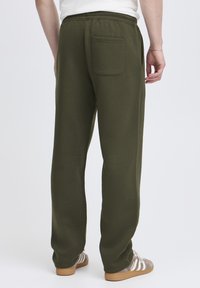 Mørkegrønne joggingbukser med elastik i taljen og en enkelt lomme bagpå; glat stof med afslappet pasform og lige ben.