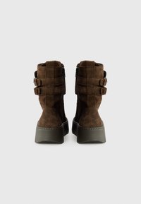 Stivaletti alla caviglia in suede marrone con suola platform chunky, dotati di cerniere e due fasce decorative sul retro. Dettaglio di superficie testurizzata.