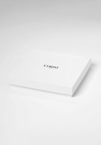 Boîte rectangulaire blanche avec une surface lisse, portant le texte "CHRIST" en police noire sur le dessus. Design simple et minimaliste.