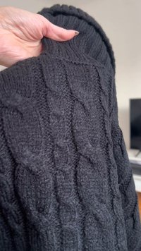 Mustat kabelikudotut neuleet, joissa on ribbikaulus. Materiaalin näyttää olevan pehmeä ja rakenteellinen, ja siinä on kohotettuja kuvioita kankaan pinnalla.