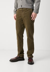 Pantalons en velours côtelé vert olive avec une coupe droite, dotés d'une fermeture à bouton et de poches avant, associés à des chaussures bourgogne foncé.
