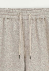 Pantalons de jogging gris clair avec une taille élastique, dotés d'un cordon de serrage avec des embouts en métal argenté et d'une surface douce et texturée.