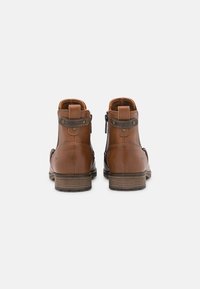 Bottines en cuir marron avec une fermeture éclair sur le côté, des coutures contrastées et un talon empilé marron. Présente une languette à l'arrière.