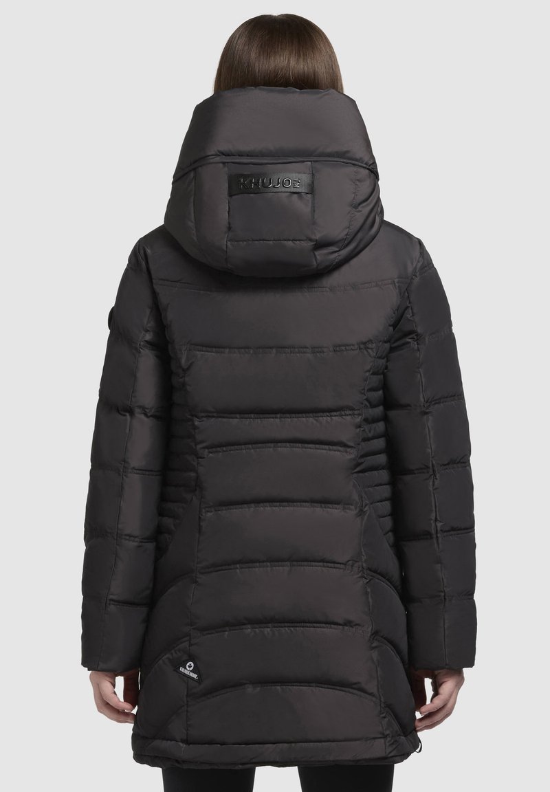 Veste rembourrée noire avec un col haut et une grande capuche, présentant des sections matelassées horizontales et un logo au niveau du cou. Texture lisse et brillante.