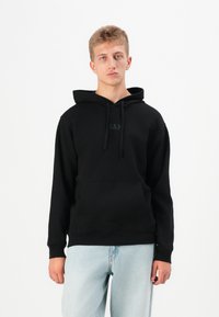 Black hoodie with a kangaroo pocket and drawstrings, featuring a subtle GAP logo on the chest. Worn with light blue jeans.