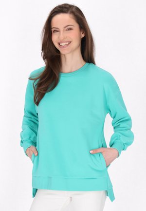 Lys teal sweatshirt med lange ærmer, rund halsudskæring, sidelommer og sideslids i kanten. Glat tekstur med en afslappet pasform.