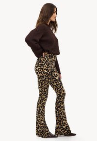 Un suéter marrón de felpa combinado con pantalones acampanados de cintura alta con estampado de leopardo. El conjunto presenta una textura suave y un audaz patrón animal.