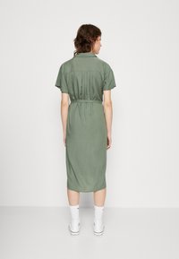 Abito midi verde khaki con maniche corte, vita aderente e taglio dritto. Indossato con sneakers bianche e calzini alla caviglia.