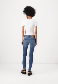 Lieknos mėlynos džinsai su aukštu liemeniu, galiniais kišenėmis ir šviesiai rudos odos etikete ant liemens. Suderinti su prigludusia balta marškinėliais ir juodais platforminiais bateliais.