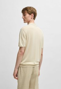 Ljust beige kortärmad polo med mjuk textur, klassisk krage och ribbade ärmslut. Buren med matchande beige texturerade byxor.