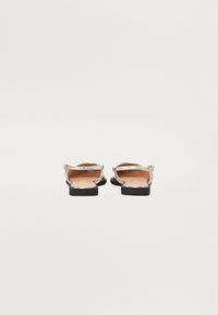 Sandales plates noires avec une boucle et une sangle argentées brillantes, dotées d'une semelle intérieure en cuir lisse et d'un design minimaliste.