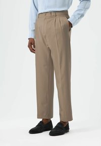 Beige pleated trousers with a tailored fit, side pockets, and a smooth texture, paired with black suede loafers.