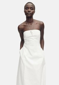 Robe blanche sans manches, faite d'un tissu lisse avec un buste structuré, des poches latérales et une silhouette droite. Design simple, accents minimalistes.