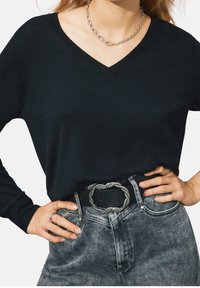 Maglione nero con scollo a V e maniche lunghe, abbinato a jeans grigi a vita alta. Presenta una cintura con fibbia decorativa argento.