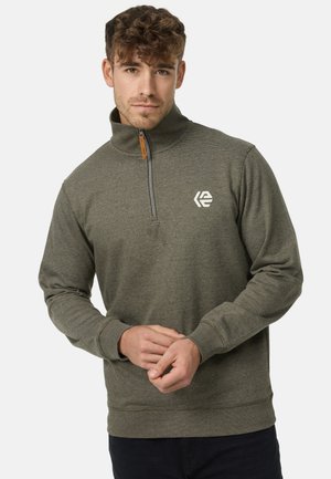 Grå hettejakke med høy krage og frontlogo. Laget av teksturert stoff, med kontrasterende glidelås og ribbestrikkede mansjetter.