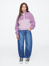 Lilla fleecepullover med høj krave, frontknaplukning og broderet logo. Parret med brede denimjeans og sorte sneakers.
