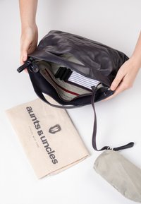 Zwarte leren schoudertas met een ritsluiting, gestreepte voering en een elastische organizer. Inclusief een beige stoffen pouch met branding.