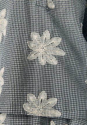 Tissu vichy bleu marine et blanc avec des fleurs blanches brodées, présentant des coutures détaillées et des centres perforés. Texture lisse, motif floral.