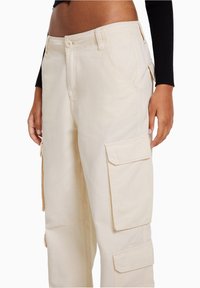 Beige cargobyxor i bomull med flera sidofickor och rak bendesign, med knappstängning och diskreta sömdetaljer.