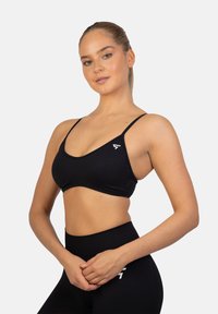 Zwarte sportbeha met dunne banden, een ronde halslijn en een wit logo aan de linkerkant; gemaakt van rekbare, gladde stof.