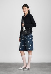 Zwarte gebreide cardigan over een witte top, denim shorts met wit bloemenpatroon, kniehoge witte sokken en zilveren puntige ballerina's.