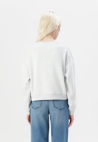 Felpa in cotone grigia con vestibilità cropped e spalle scese, caratterizzata da polsini e orlo a coste, abbinata a jeans in denim blu chiaro.