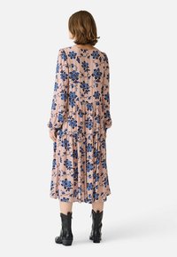Flödande rosa klänning med blå blommönster, långa ärmar och vågig nederkant. Buren med svarta cowboyboots. Mjuk tygtextur.