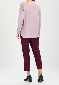 Suéter de canalé color púrpura claro con mangas largas, combinado con pantalones pitillo color berenjena y zapatos de tacón bloque verde. Fondo liso.