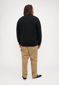 Sort strikketrøje, beige cargos med sidelommer og sorte sneakers med hvide såler. Simpelt, casual design i neutrale farver.