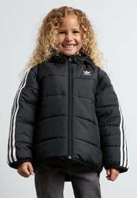 Casaco puffer preto com fecho na frente, capuz e riscas brancas nas mangas. Apresenta um acabamento texturizado e um logótipo bordado no peito.