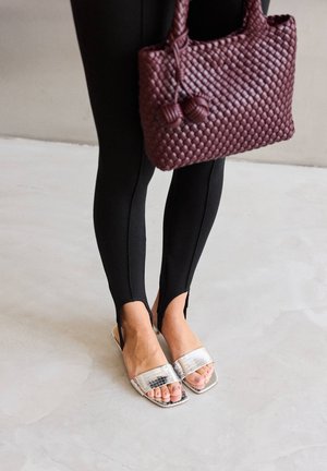 Legs in black leggings with front slits at ankles, wearing silver square-toe slide sandals, holding a textured purple handbag.