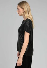 T-shirt noir à manches courtes avec une texture brillante, encolure ronde et coupe décontractée, associé à un pantalon noir.