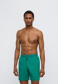 Πράσινα μαγιό σορτς από ελαφρύ ύφασμα, με ελαστική μέση και κορδόνι. Λείο ύφασμα, μήκος έως το γόνατο.