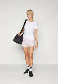 Must have sportlik kott, valge T-särk musta logoga, heledad roosa aluspüksid, mustad jooksujalad ja triibulised sokid on seljas inimesel.