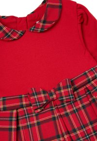 Rotes Kleid mit kariertem Kragen und plissiertem Rock. Der Rock ist mit einer Schleifendetail versehen, das einen Kontrast zur glatten Textur des Oberteils bildet.