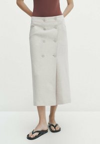 Linnen midi-rok in lichtbeige met dubbele knoopsluiting, zijzakken en een klassieke wikkelontwerp. Gepaard met zwarte teenslippers.