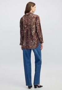 Leopardprint langemouwhemd in tan en bruin tinten, gecombineerd met hoge taille spijkerbroek in het blauw en zwarte hakken. Getextureerde stof.