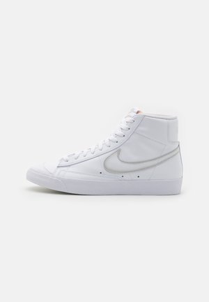 Hightop tenisky vyrobené z bílé kůže s textura, s černým Nike Swoosh a bílými tkaničkami, na ploché gumové podrážce.