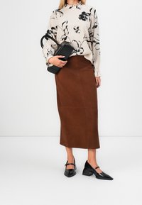 Bluse i beige med blomsterprint og lange ærmer; brun ruskind, knælang nederdel; sort struktureret håndtaske; sorte spidse sko med remme.