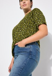 Camiseta de manga corta con estampado de leopardo verde, hecha de una tela suave, combinada con unos pantalones vaqueros de mezclilla azul de cintura alta. Diseño minimalista con bolsillos funcionales.