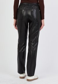 Zwarte leren broek met een gladde textuur, met een middelhoge taille, achterzakken en een recht gesneden ontwerp, gecombineerd met witte schoenen.